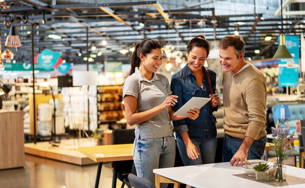 Cheerful sales woman showing a design on tablet to mid adult couple looking for furniture at a home store